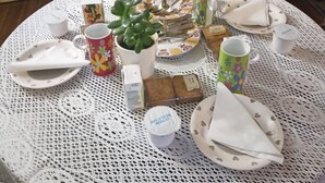 Una mesa redonda con mantel de encaje, rodeada de vajilla variada y una pequeña planta en maceta.
