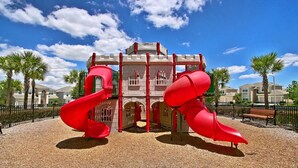 Une aire de jeux avec deux toboggans rouges et une structure ressemblant à un château.