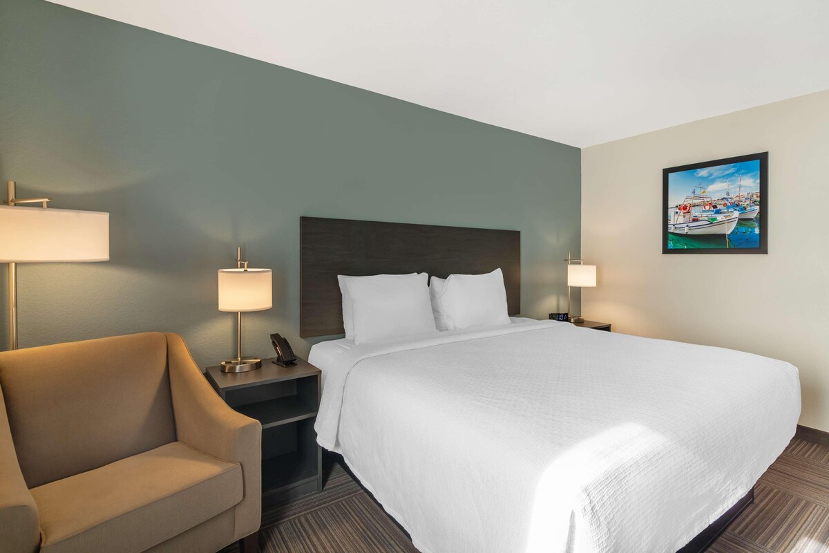 Une chambre d’hôtel avec un grand lit, deux tables de chevet avec des lampes, une chaise et un tableau au mur.