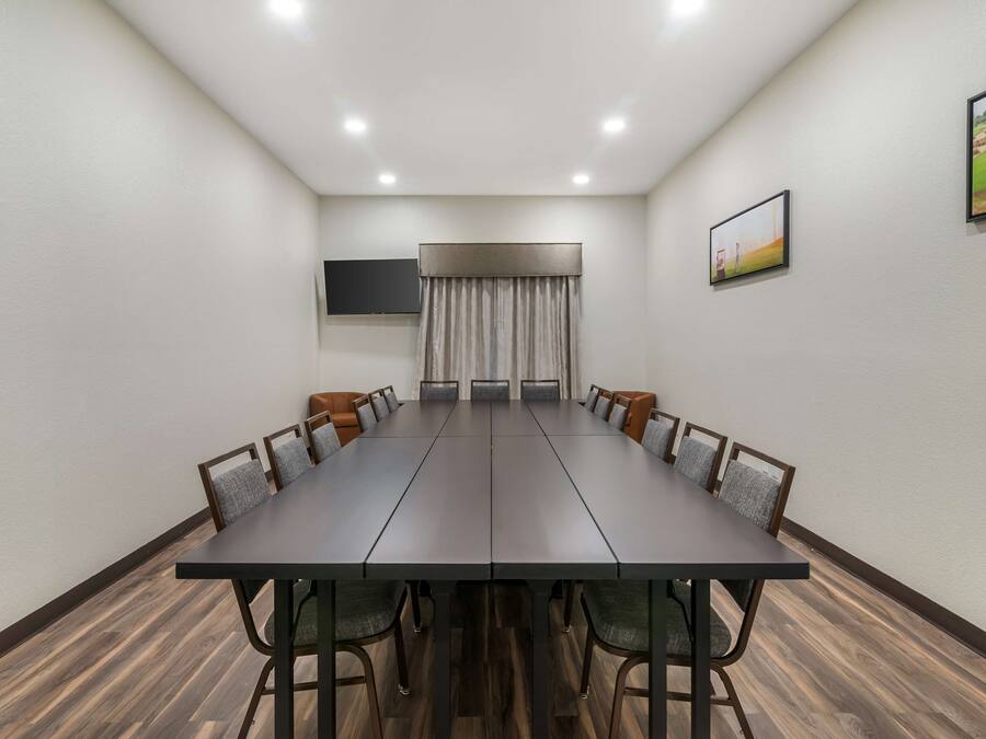 A conference room with a long table, chairs, a flat-screen TV, and a window with curtains.