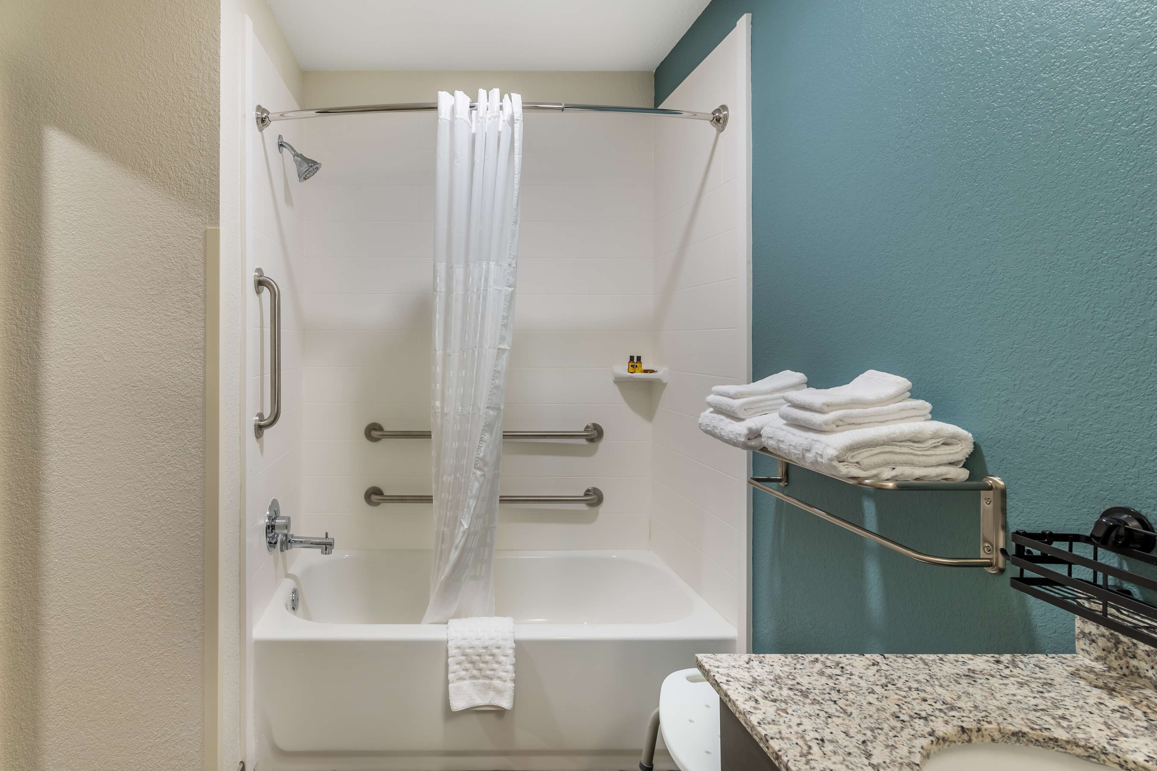 Un baño con ducha, barras de apoyo, toallero y retrete.