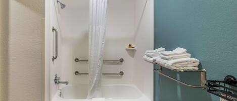Un baño con ducha, barras de apoyo, toallero y retrete.