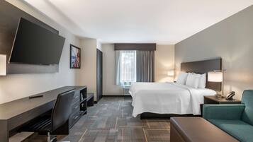 A hotel room with a bed, a desk, a chair, a TV, a lamp, and a couch.