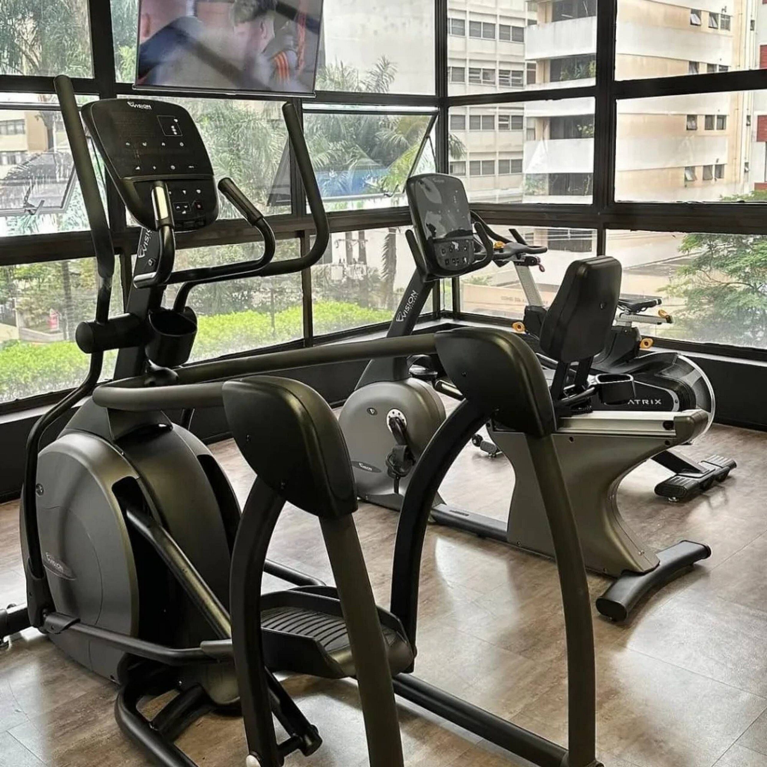 Ein Fitnessstudio mit Laufbändern und Trainingsgeräten, große Fenster mit Blick auf Gebäude und Grünflächen.