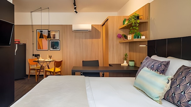 A modern hotel room with a large bed, a dining area, and a TV. - Get a Flat 120 Luxuoso-Jardins (São Paulo)