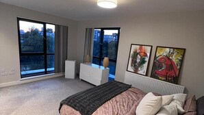 Een slaapkamer met een groot bed, een kaptafel en een raam met uitzicht op gebouwen en bomen.