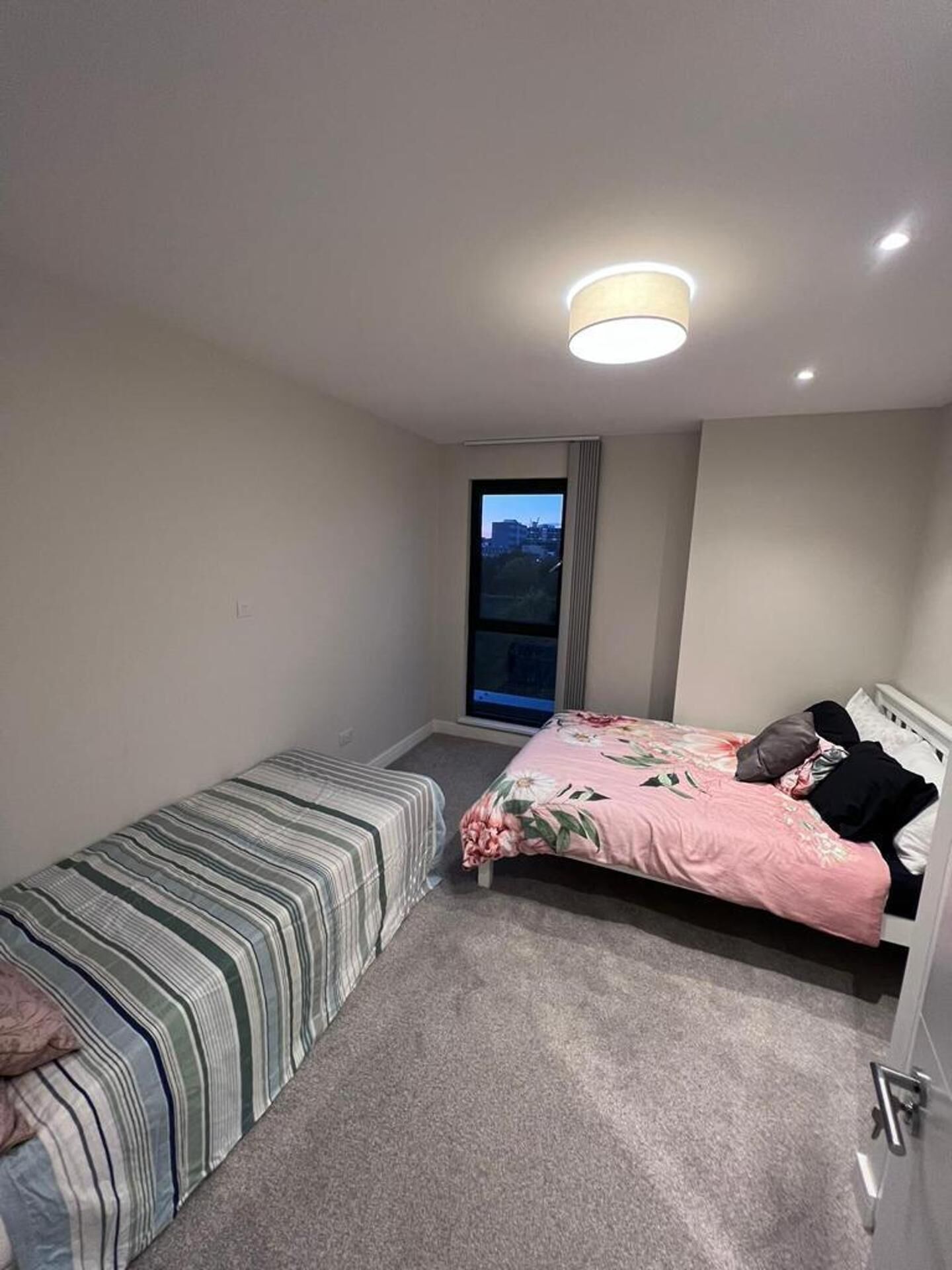 Een kleine, goed verlichte slaapkamer met een enkel bed, een kleintje en een raam met uitzicht.