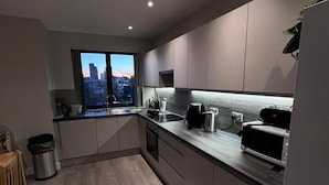 Een moderne keuken met uitzicht op de stad door een groot raam, voorzien van een fornuis, magnetron en gootsteen.