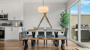 A modern kitchen with white cabinets, a built-in microwave, and a dining area with a wooden table and chairs. - Wanderer`s Haven | Private Nordic Spa | Game Room (Cochrane)