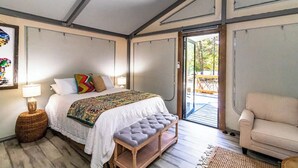 A bedroom with a bed, bedside lamps, a bench, a chair, and a view of the outdoors.