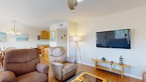 A living room with a flat-screen TV, two leather sofas, a dining area with wooden chairs, and a kitchen in the background. - Beach Access Across the Street, Shared Heated Pool (Corpus Christi)