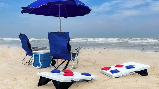 A beach setup with a blue umbrella, two beach chairs, a cooler, and two shuffleboard tables. - Beach Access Across the Street, Shared Heated Pool (Corpus Christi)