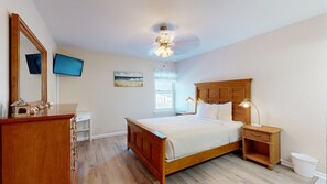 A bedroom with a wooden bed, bedside lamps, a ceiling fan, a TV, a window, and a small table with decorative items. - Beach Access Across the Street, Shared Heated Pool (Corpus Christi)