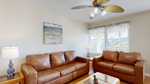 A living room with two brown leather sofas, a coffee table, a floor lamp, a ceiling fan, and a window with blinds. - Beach Access Across the Street, Shared Heated Pool (Corpus Christi)