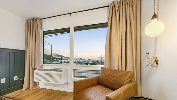 A room with a large window, a brown leather chair, a standing heater, and a lamp. - Comfort, Style & Views | Steps to Tours & Eats (Juneau)