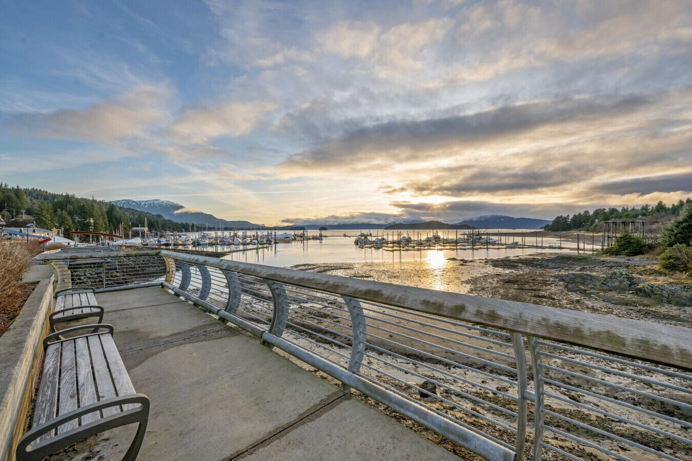 A waterfront promenade with benches and a railing overlooking a marina.