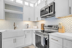 Una cocina moderna con armarios blancos, horno empotrado, microondas y cafetera.