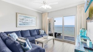 Una sala de estar con un sofá azul, una mesa de centro y vista al océano a través de amplias ventanas.