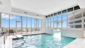 Una piscina interior con agua cristalina, ventanas amplias y vistas a la playa.