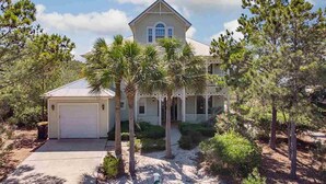 A two-story house with a garage, surrounded by palm trees and pine trees. - Sea La Vie Martinique on the Gulf Sleeps 11 (Gulf Shores)