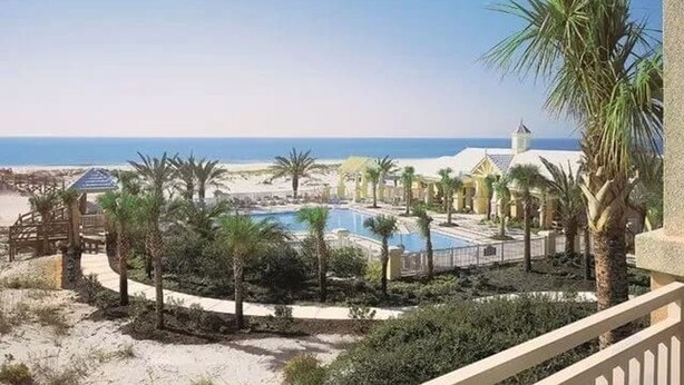 A resort with a pool, palm trees, and a beach view. - Sea La Vie Martinique on the Gulf Sleeps 11 (Gulf Shores)