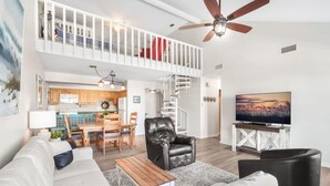 A spacious living area with a sofa, a coffee table, a black leather chair, a TV, and a staircase leading to an upper level. - Cotton Bayou 2H 3BR With Loft (Orange Beach)