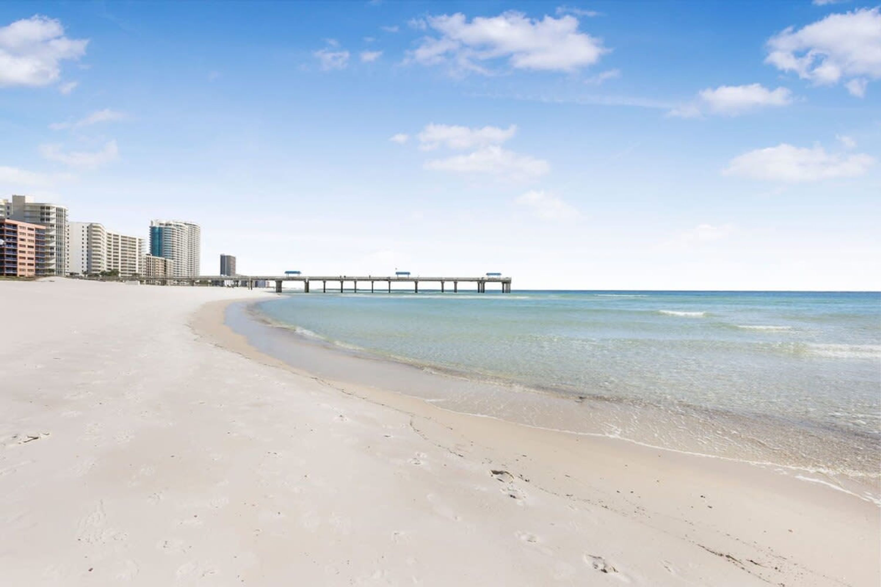 A beach with a pier extending into the ocean, surrounded by high-rise buildings.