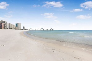 A beach with a pier extending into the ocean, surrounded by high-rise buildings.