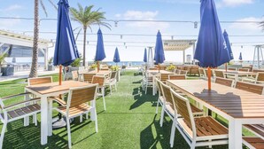 An outdoor seating area with tables and chairs, blue umbrellas, and a view of the ocean. - Cotton Bayou 2H 3BR With Loft (Orange Beach)