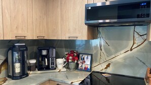 A kitchen with a stainless steel microwave, a coffee maker, a wine cooler, and a framed photo on the counter. - Rustic Elegance- Private Heated Salt pool, 2 bed, 2 bath, Fenced & Pet friendly (Port St Lucie)