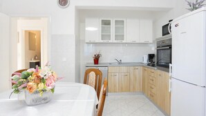 Una cocina moderna con armarios blancos, un microondas y un refrigerador. Hay una mesa de comedor con sillas y un florero con flores.