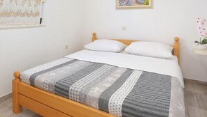 Un dormitorio con cama de madera, ropa de cama blanca, un cuadro en la pared y una ventana con cortinas de gasa.