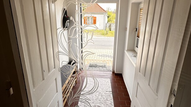 A hallway with white doors, a metal gate, and a view of a house with a red roof.