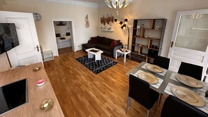 A modern living room with a wooden floor, a sofa, a coffee table, a dining table with chairs, and a chandelier.
