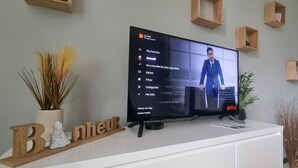 Un téléviseur fixé sur un meuble blanc, dont l’interface Netflix affiche un homme en costume.