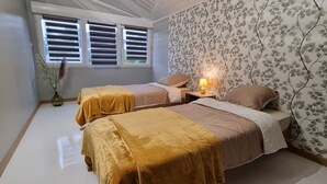 Une chambre avec deux lits, une table de chevet avec une lampe, une fenêtre avec des stores et un papier peint à motifs floraux.
