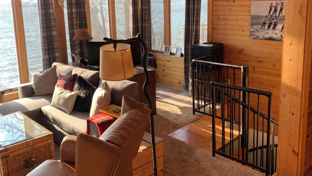 A cozy cabin with a wooden interior, a sofa, a lamp, a TV, and a view of the lake. - German lake Family Adventures

 (Waterville)