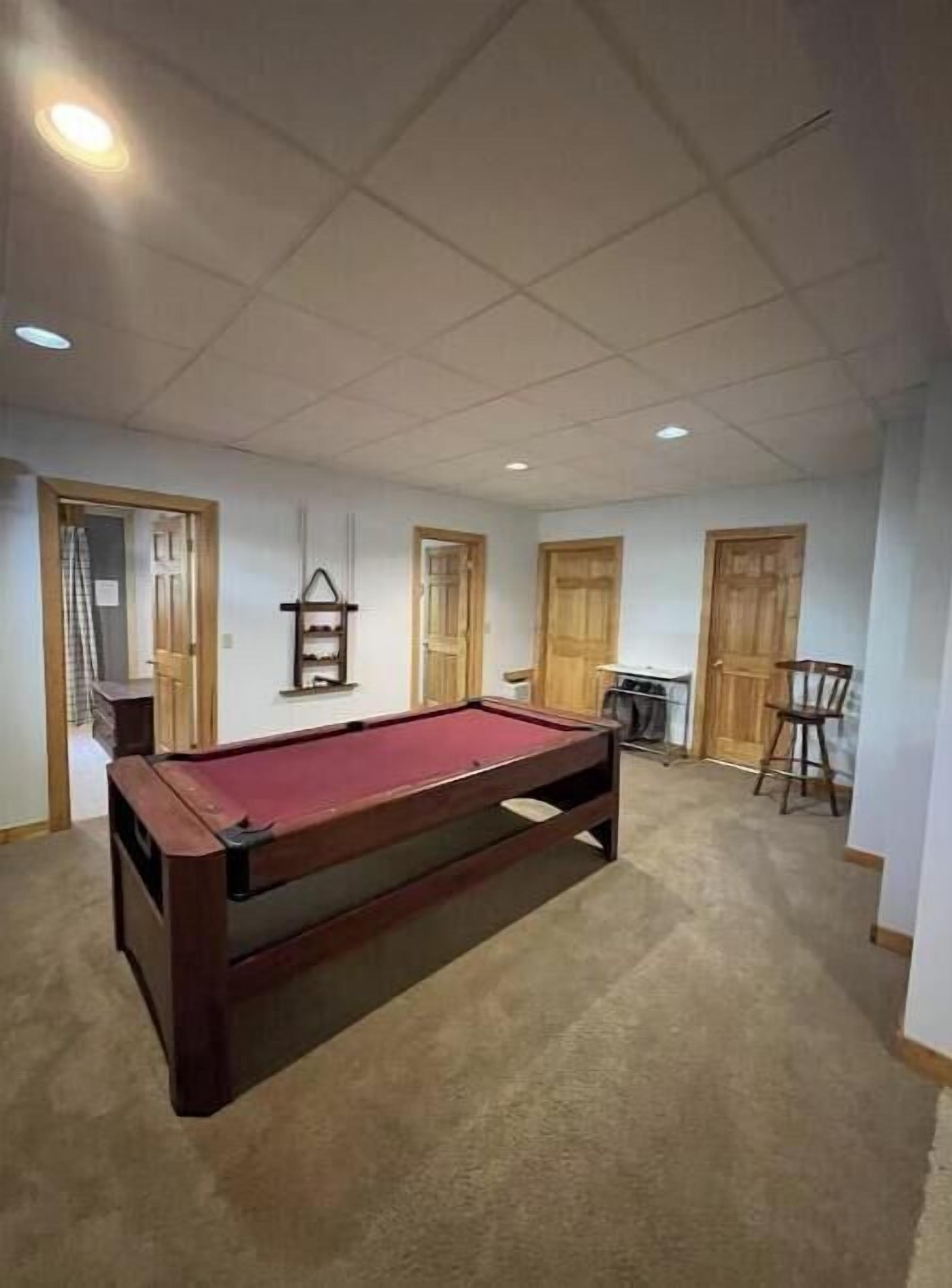 Una habitación con mesa de billar, puertas de madera, una mesita y una silla.