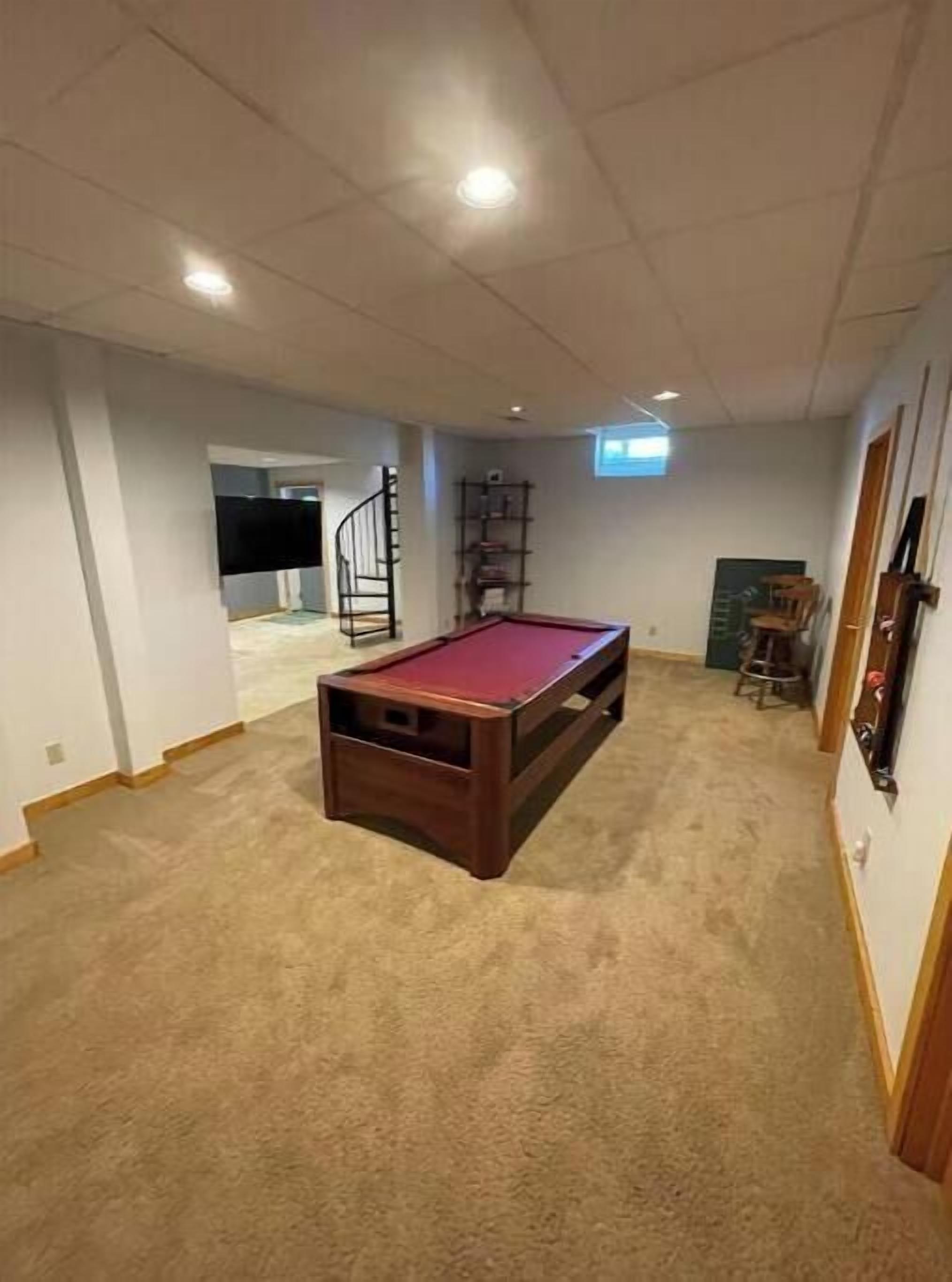 Una habitación con mesa de billar, piso alfombrado y una escalera que conduce a otra zona.