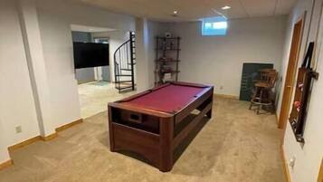 Una habitación con mesa de billar, piso alfombrado y una escalera que conduce a otra zona.