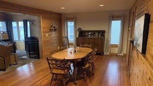 A spacious dining area with a wooden table and chairs, a kitchen in the background, and a view of the outdoors through large windows. - German lake Family Adventures

 (Waterville)
