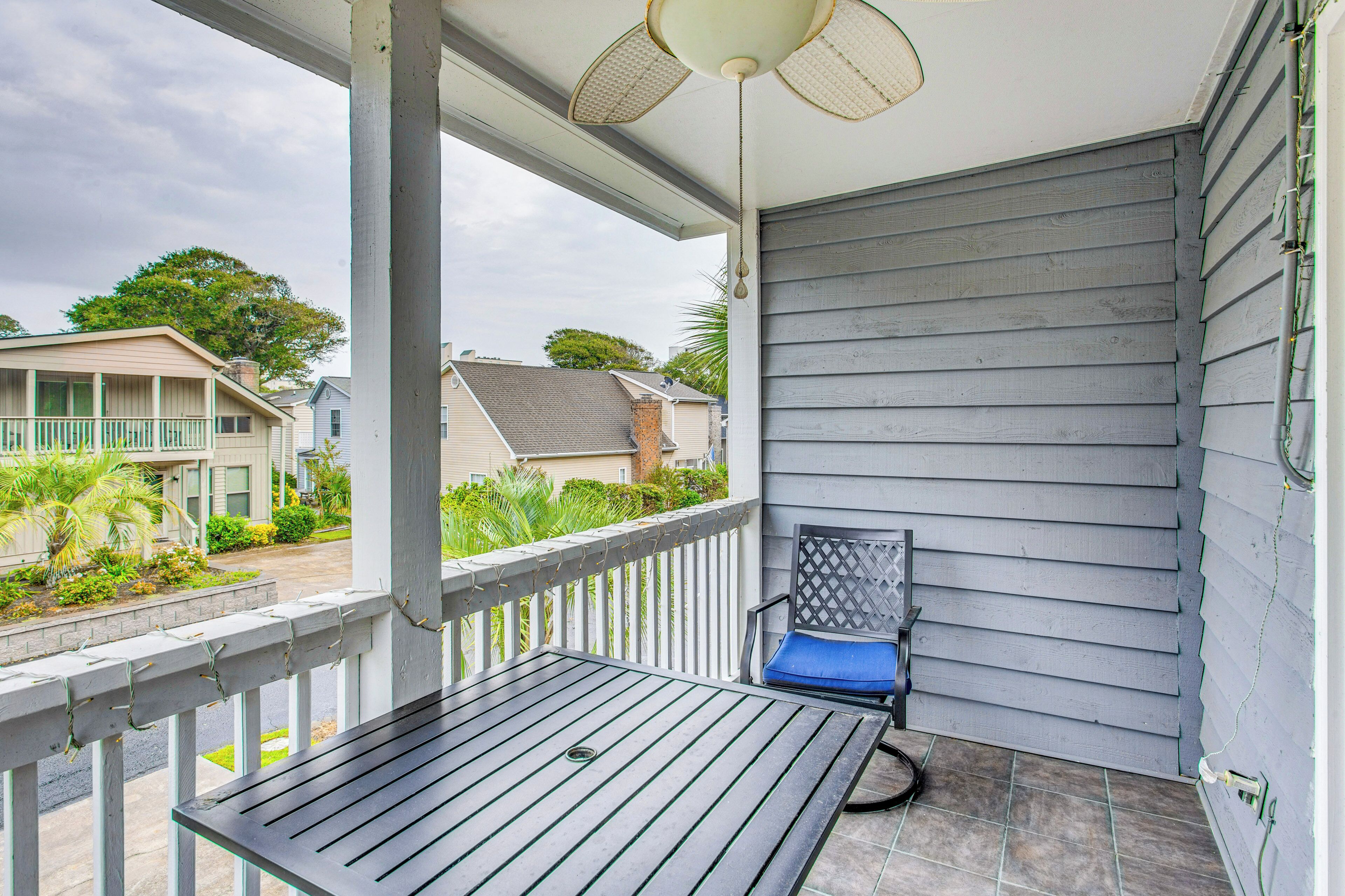 A balcony with a table and a chair, a ceiling fan, and a view of neighboring houses.