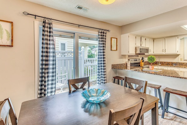 A dining area with a table, chairs, and a blue glass bowl. There is a kitchen area with cabinets and a microwave. - North Myrtle Beach Home 2 Blocks to Ocean! (North Myrtle Beach)