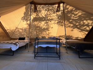 Una carpa con dos camas, una mesa y luces colgantes.