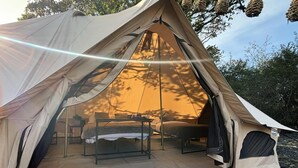 A large tent with a table and two beds inside, set on a stone path with trees in the background. - Cozy Winter Hot Tent With Log Burner, Tv & Hot tub (Llanfairpwllgwyngyll)