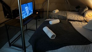 A cozy tented accommodation with two beds, a television, and a small table. - Cozy Winter Hot Tent With Log Burner, Tv & Hot tub (Llanfairpwllgwyngyll)