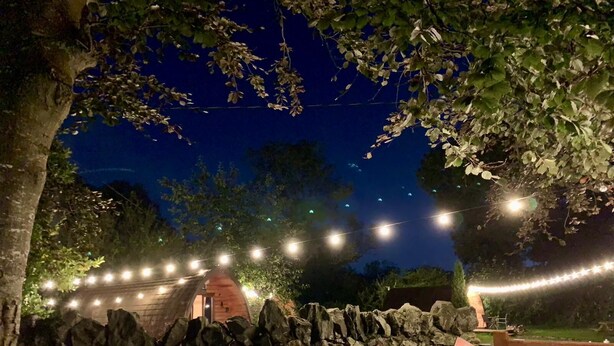 A stone wall with a rustic brick structure, string lights, and a wooden gate. - Cozy Winter Hot Tent With Log Burner, Tv & Hot tub (Llanfairpwllgwyngyll)