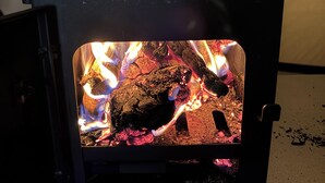 A wood-burning stove with visible flames and logs inside. - Cozy Winter Hot Tent With Log Burner, Tv & Hot tub (Llanfairpwllgwyngyll)