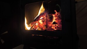 A wood-burning stove with visible flames and logs inside. - Cozy Winter Hot Tent With Log Burner, Tv & Hot tub (Llanfairpwllgwyngyll)