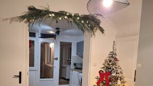 Una sala moderna con suelo de madera, un sofá gris, una mesita redonda y un árbol de Navidad con adornos rojos.